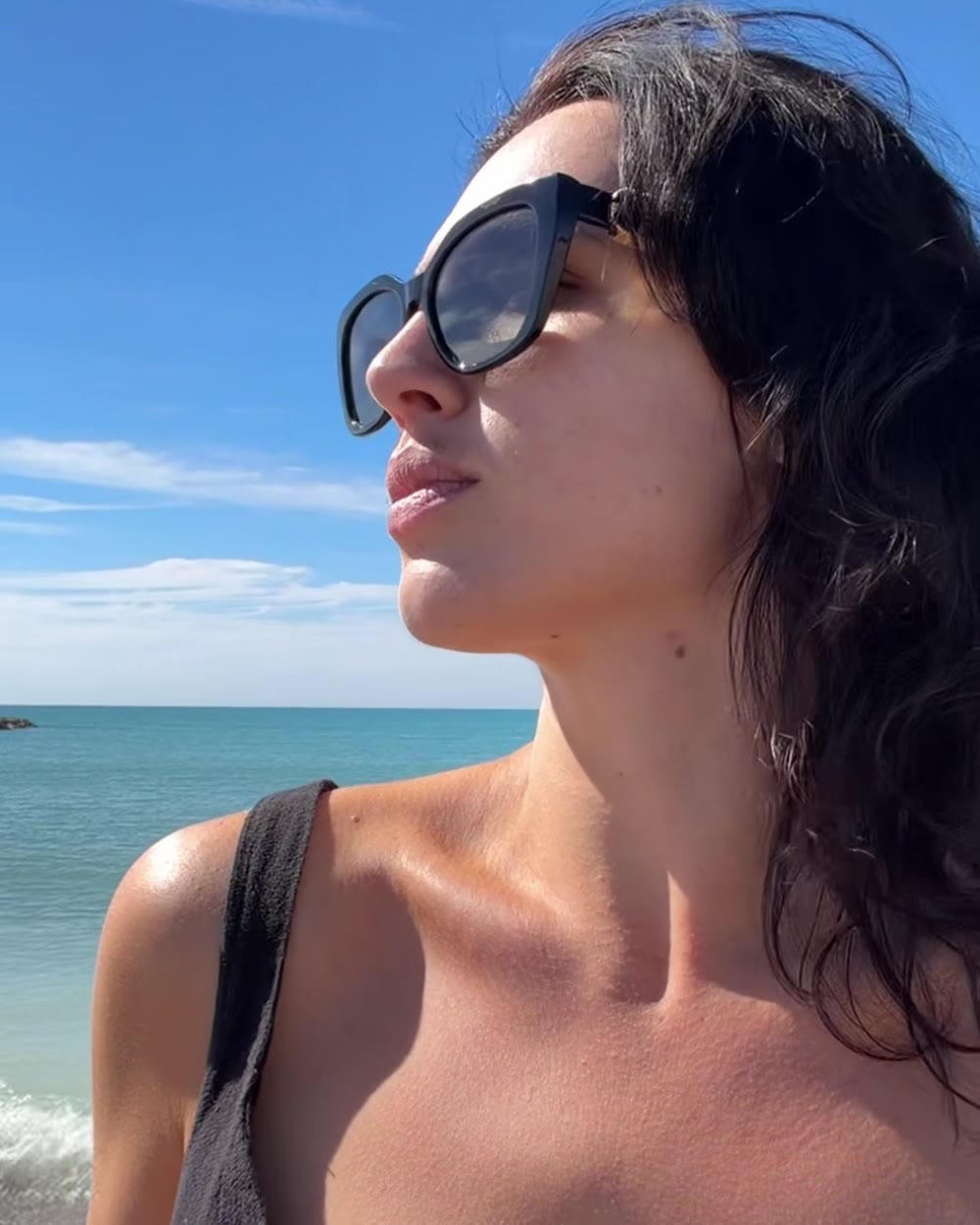 Esther in sunglasses on the beach, looking out at the sea